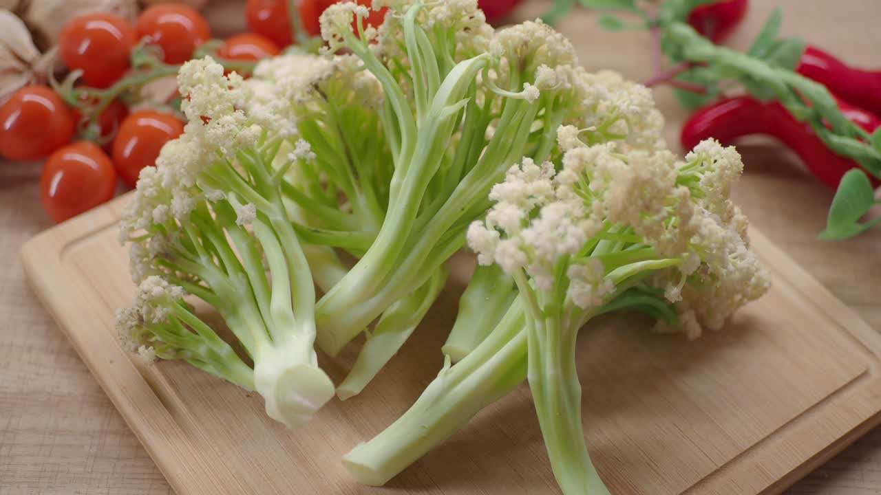Cimette di cavolfiore crudo e verdure fresche su un tagliere di legno.