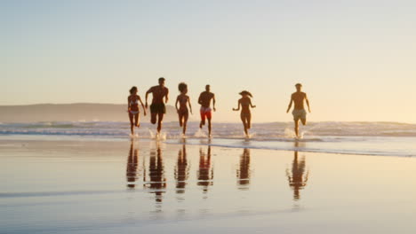 friends running through waves at sunset on beach vacation