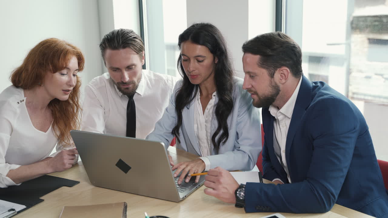 A young work team composed of two women and a man discusses financial matters around a laptop at a business meeting.