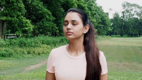 kolkata,india:-calm young woman taking deep breath of fresh air relaxing meditating with eyes closed enjoying peace, serene indian girl doing yoga pranayama exercise feel no stress free relief