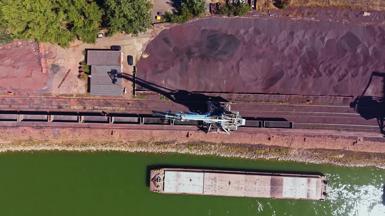 Attrezzature da costruzione caricano materiali su una chiatta vicino a una sponda del fiume in un'area industriale durante le ore diurne.