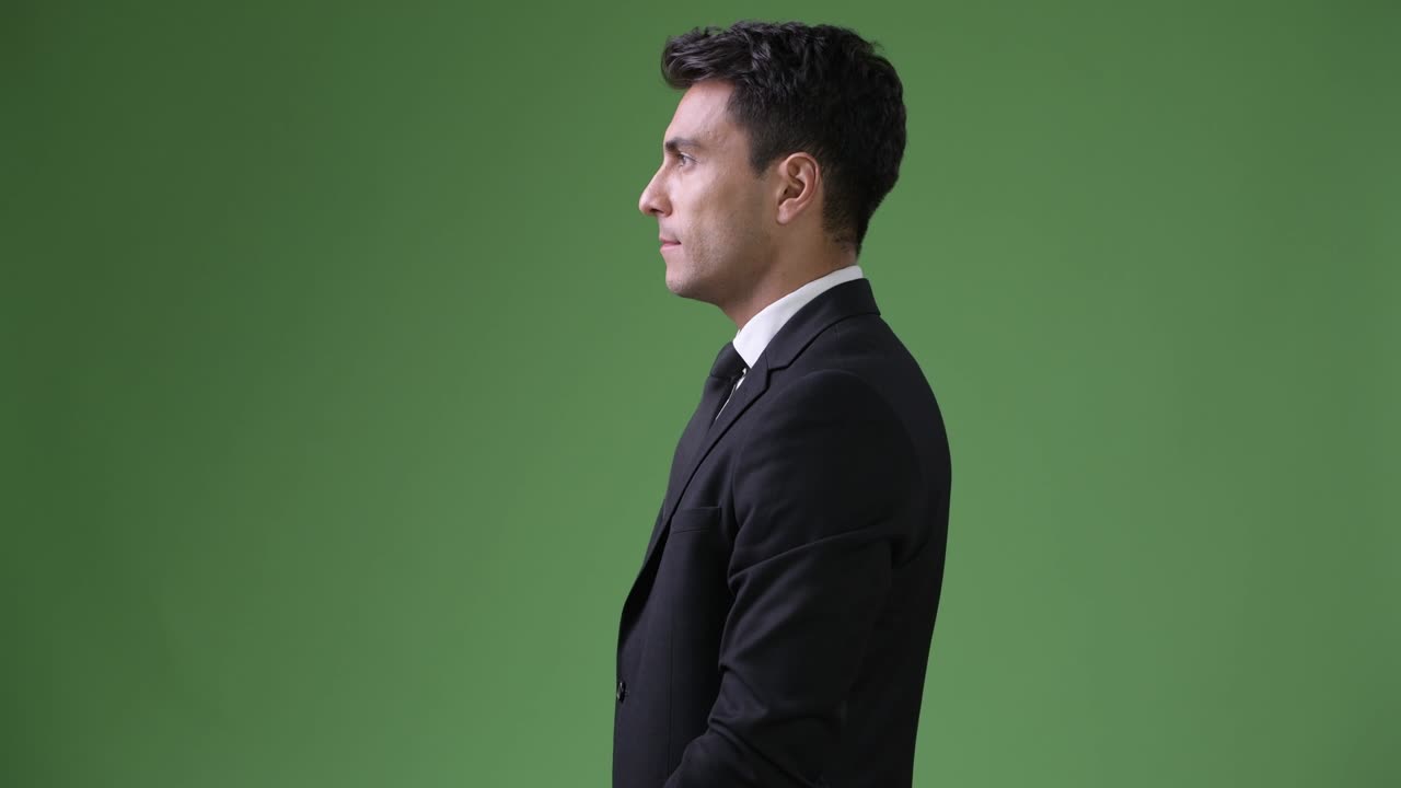 Young handsome Hispanic businessman against green background