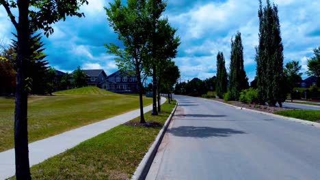 nubes blancas azules de verano que se forman en un camino misterioso que conduce a algunas casas de lujo masivas en una tarde ventosa y brillante con hileras de árboles altos y verdes que revelan el zoom óptico en el camino de entrada