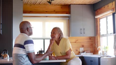 Feliz-Pareja-Afroamericana-Mayor-Tomando-Café-Y-Hablando-En-La-Cocina,-Cámara-Lenta