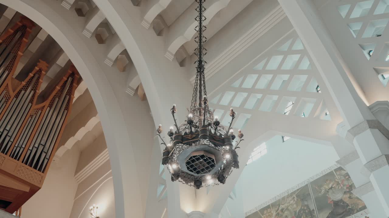 Ornate chandelier hanging from the ceiling of a cathedral with visible organ pipes in the background
