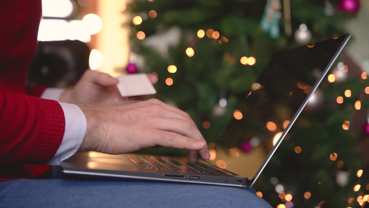 크리스마스 장식이 있는 거실의 크리스마스 트리 근처에 앉아 있는 그녀의 다리 위에 노트북에 타이핑하는 사람의 손을 클로즈업