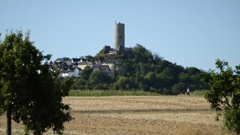 Lapso-De-Tiempo-De-Las-Ruinas-Del-Castillo-De-Vetzberg-Que-Se-Elevan-Sobre-Una-Pequeña-Colina-Con-Pocas-Casas-De-Pueblo-Alemanas-Y-Campos-De-Grano-Seco-Debajo