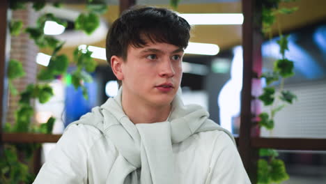 white man in white shirt and tying white sweater looking boldly into friend eyes during intense conversation, closeup on face showing confidence and connection in casual indoor setting