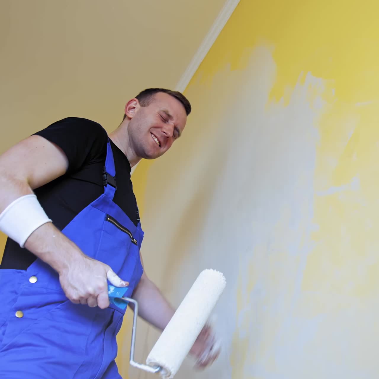 Man having fun during painting room. Professional young happy man with paint roller having fun