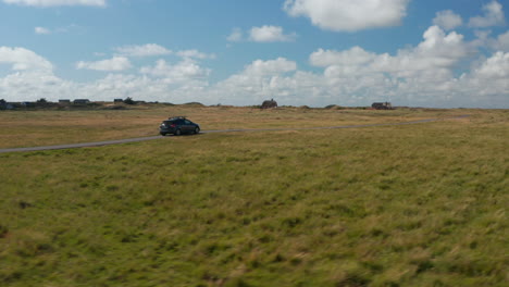 Tracking-of-car-driving-on-narrow-pathway-in-countryside.-Vast-flat-grasslands-with-several-buildings.-Denmark
