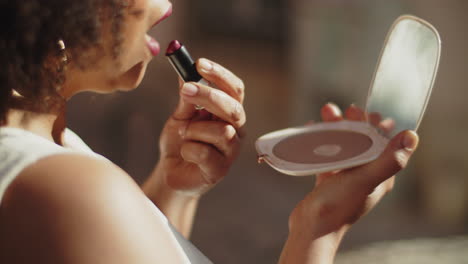 primer plano de una novia afroamericana mirando en el espejo y aplicando lápiz labial antes de la ceremonia de boda