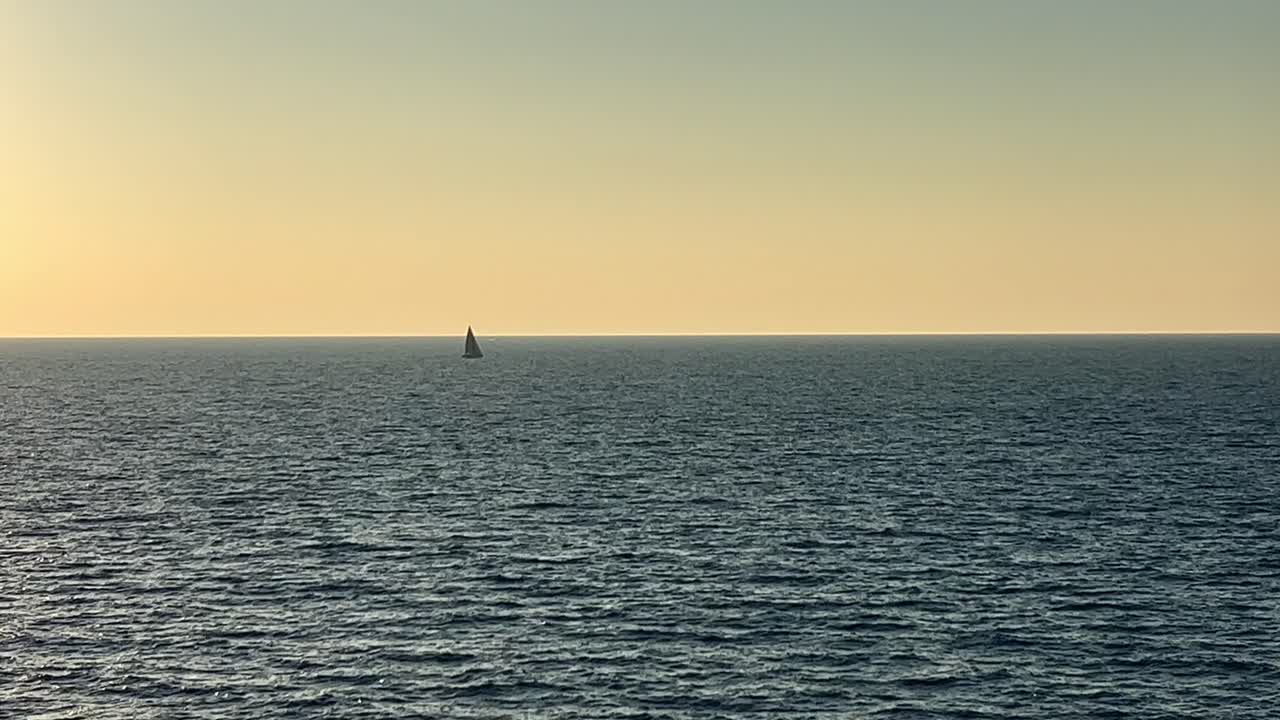 해가 지는 동안 열린 바다에서 항해하는 멀리 있는 세일보트