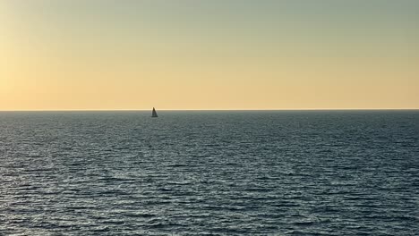 Sailboat-in-the-distance-sailing-on-open-sea-at-sunset