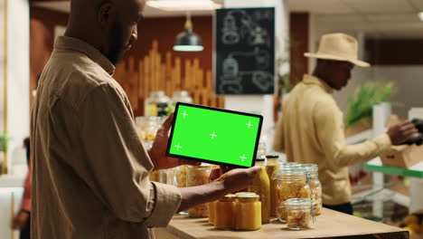 un comprador afroamericano muestra una tableta con una plantilla de pantalla verde en una tienda de comestibles