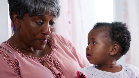 smiling grandmother cuddling baby granddaughter at home