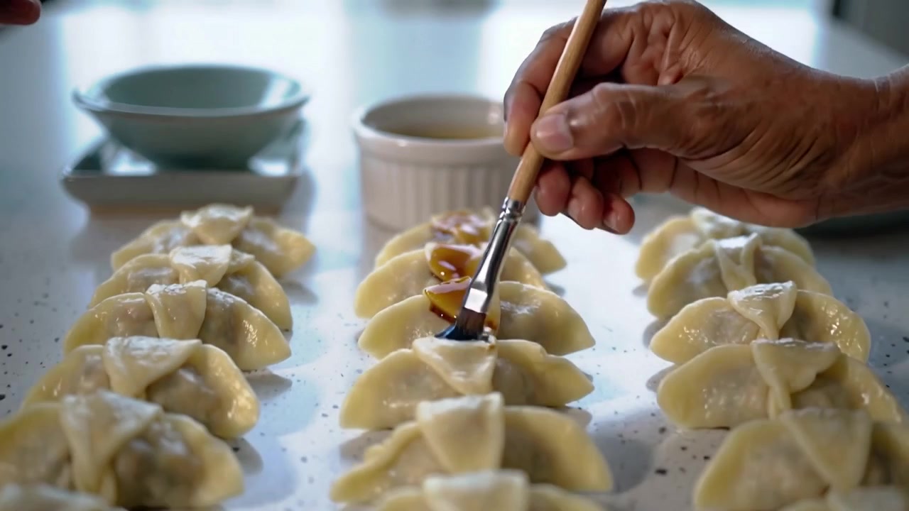 Picking cook dipping brush in ramekin on home counter, glazing center dumpling row to add shine