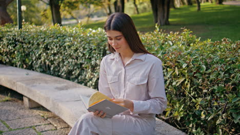 romantic girl reading book in green park. relaxed student study sitting bench