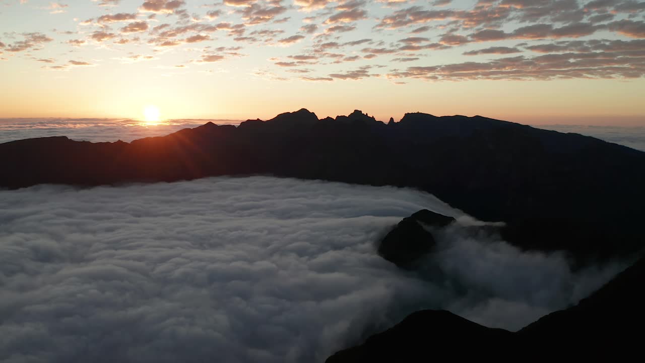 Mare di nuvole scorre tra montagne scure durante un'alba colorata, vista aerea