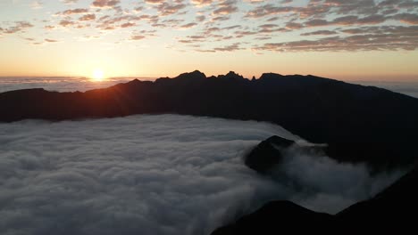 sea of clouds flows between dark mountains during colorful sunrise, aerial