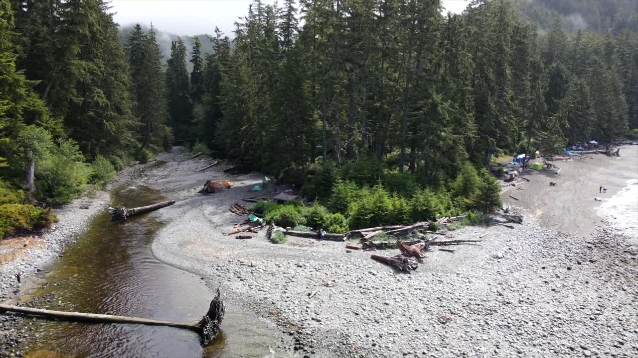 Ascending aerial dronie shot on Sombrio beach revealing heavy fog above vast and lush coniferous forest bordering the pacific coast