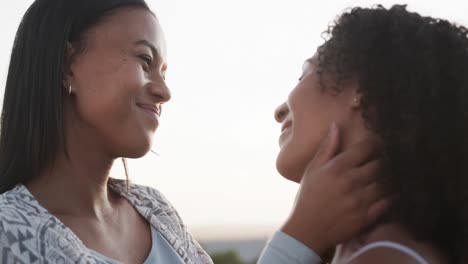 Romantic-biracial-lesbian-couple-smiling-and-embracing-in-garden-at-sundown,-slow-motion