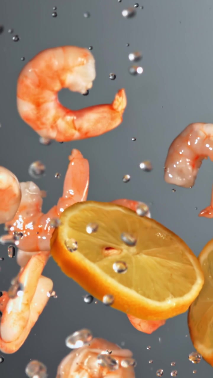 Gamberi freschi e fette di limone che cadono nell'acqua al rallentatore