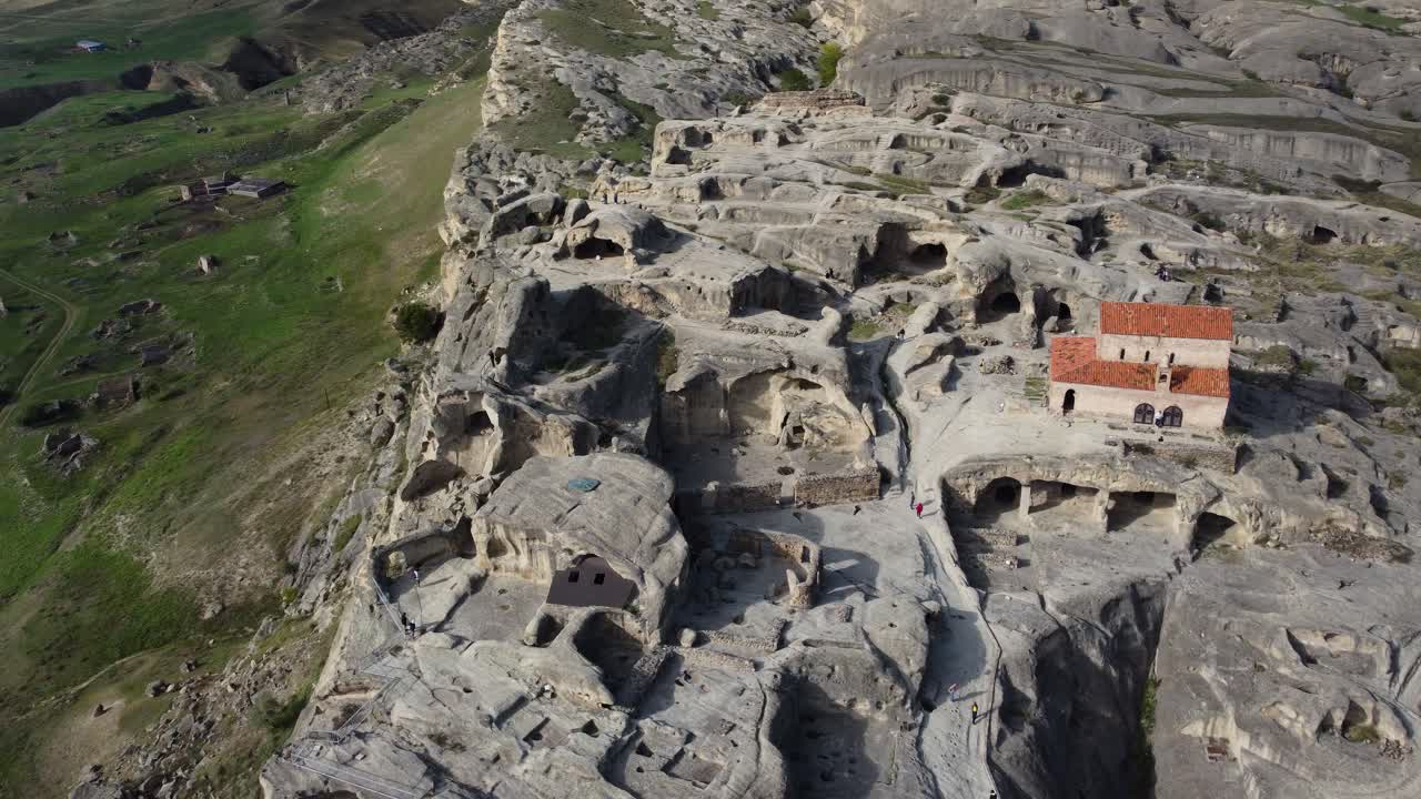 Aerial over ancient Uplistsikhe rock city with church on hill and caves below