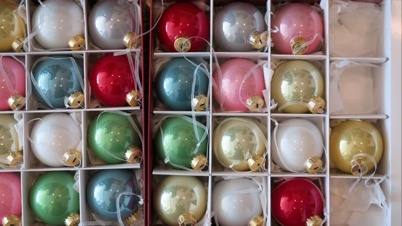 Overhead perspective of a hand placing colorful Christmas tree balls back into a box after the holidays