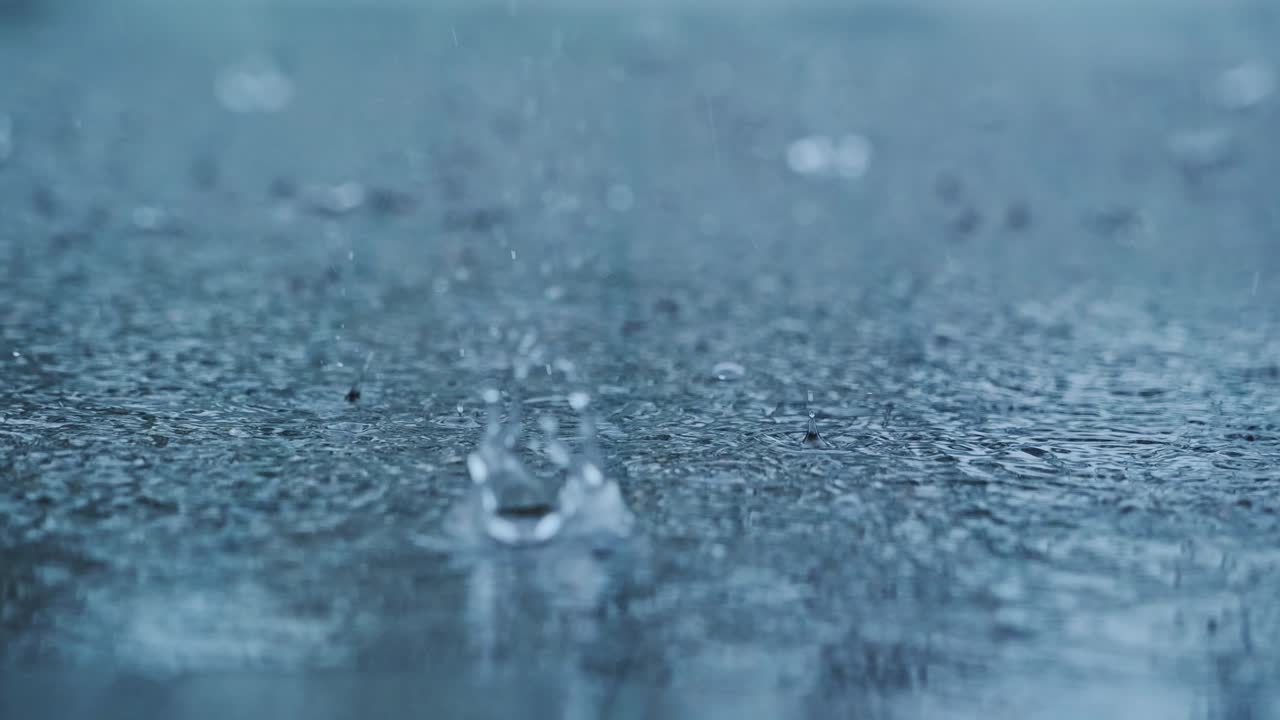 Cinematic macro shot of raindrops bursting on pavement in stormy weather