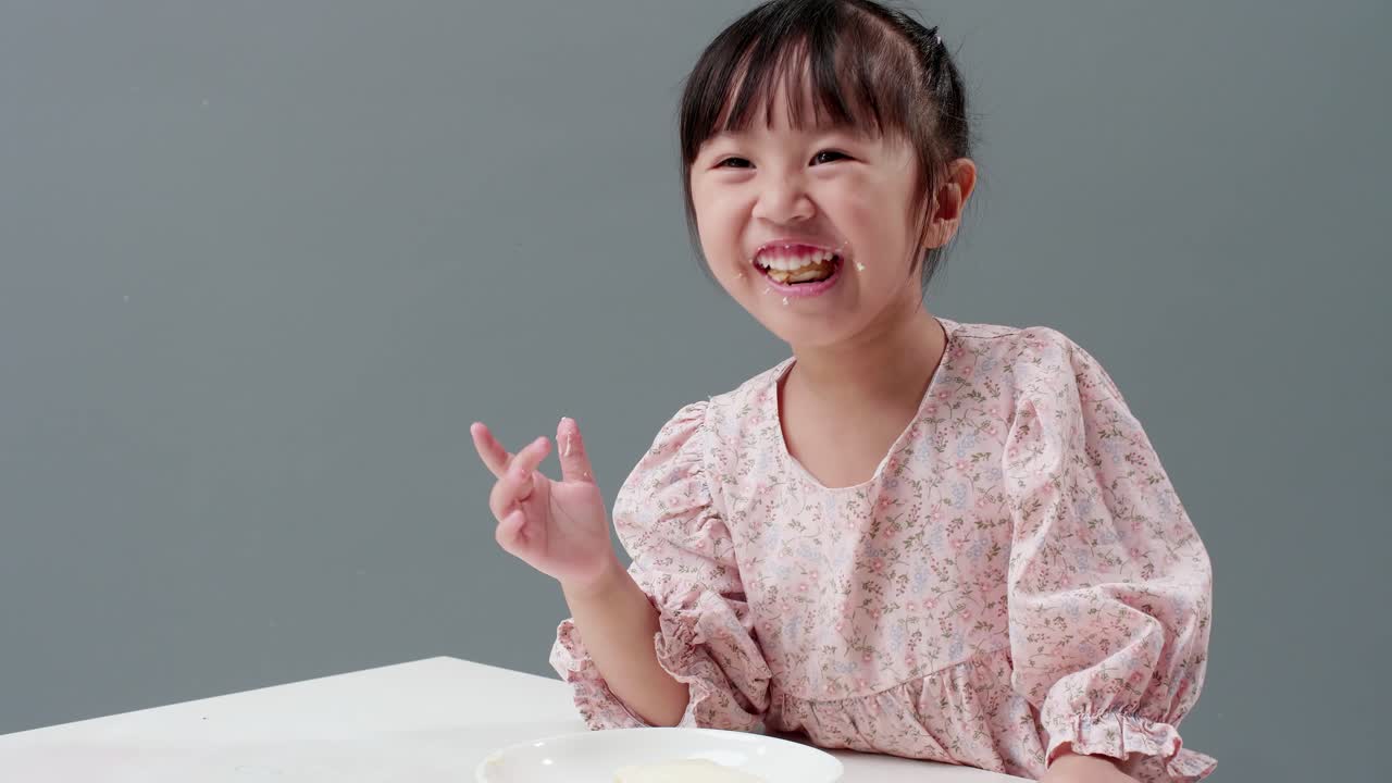 회색 배경을 가진 스튜디오에서 달콤한 조각을 먹는 아시아 어린이