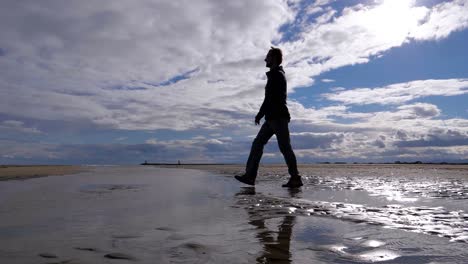 Slow-motion-shot-of-a-man-walking-along-a-beach-near-the-Sete-Salt-Flats