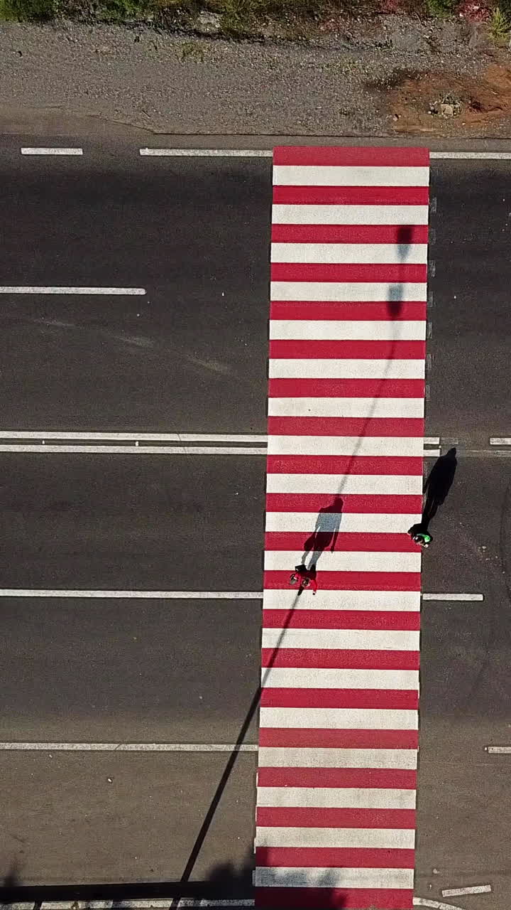 people are crossing the road on a pedestrian of red and white color on the background of the car. Aerial view Vertical video