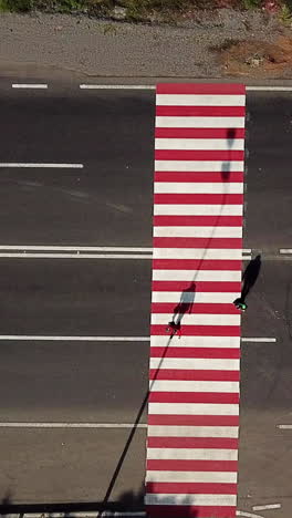 people are crossing the road on a pedestrian of red and white color on the background of the car. aerial view vertical video