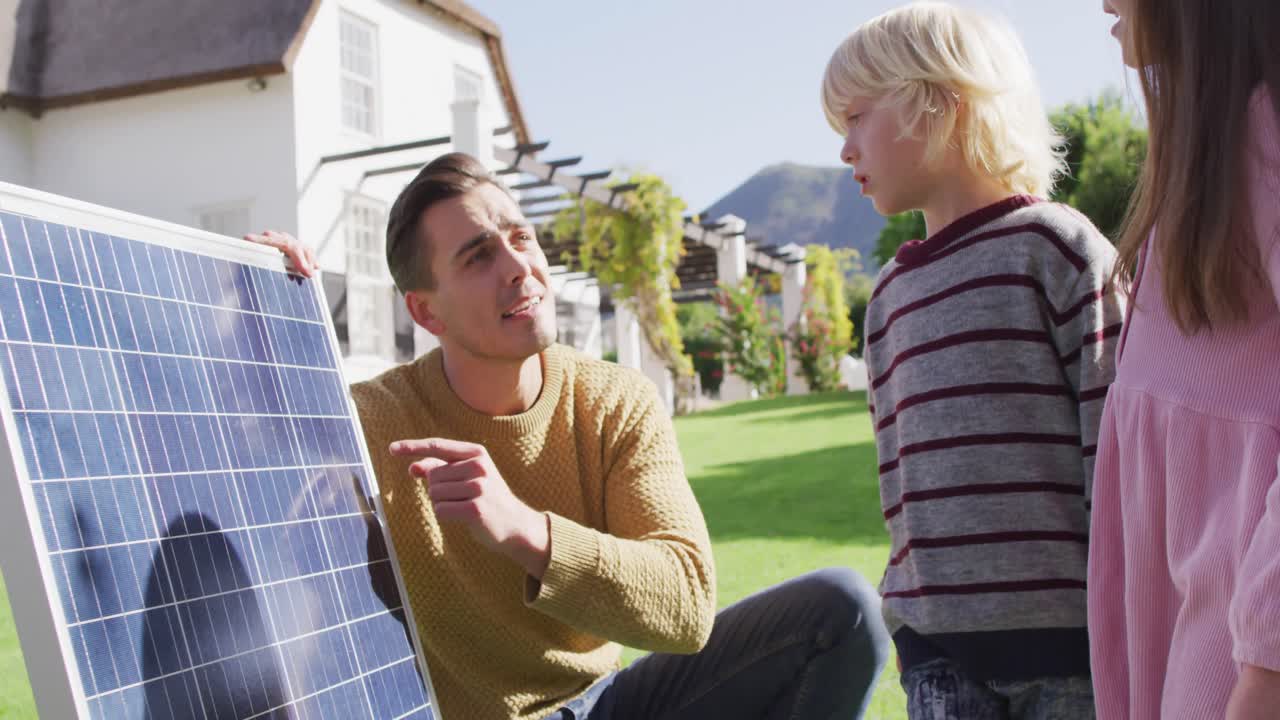 Video of happy caucasian father explaining solar panel to son and daughter in sunny garden