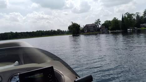 a cottage country lake is viewed from inside a moving pontoon boat.