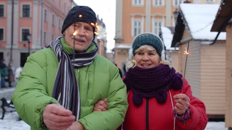 Senior-happy-couple-with-burning-sparklers-bengal-lights-celebrating-birthday-on-city-center-street