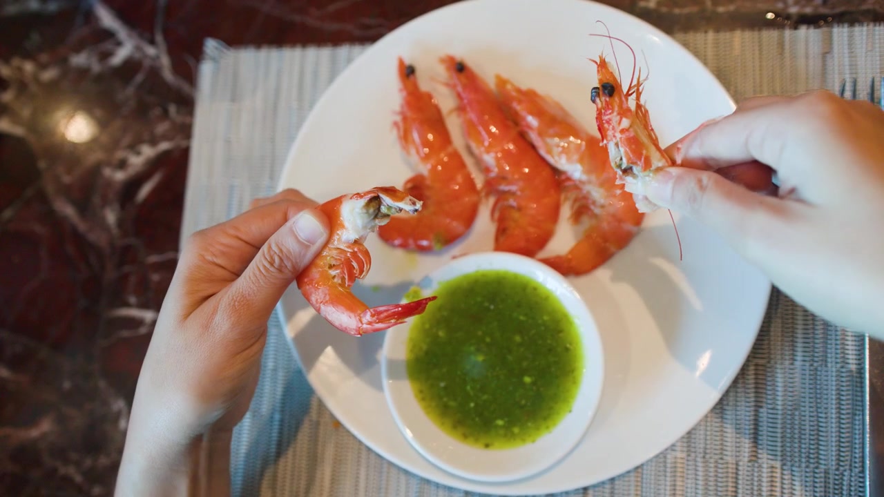 Vista dall'alto di mani che sbucciano gamberi cotti serviti con salsa piccante al peperoncino verde thailandese.