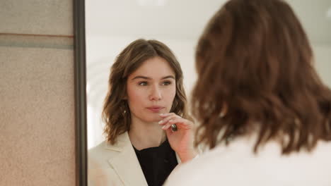 Woman-looks-in-mirror-touching-skin-and-adjusting-hairstyle