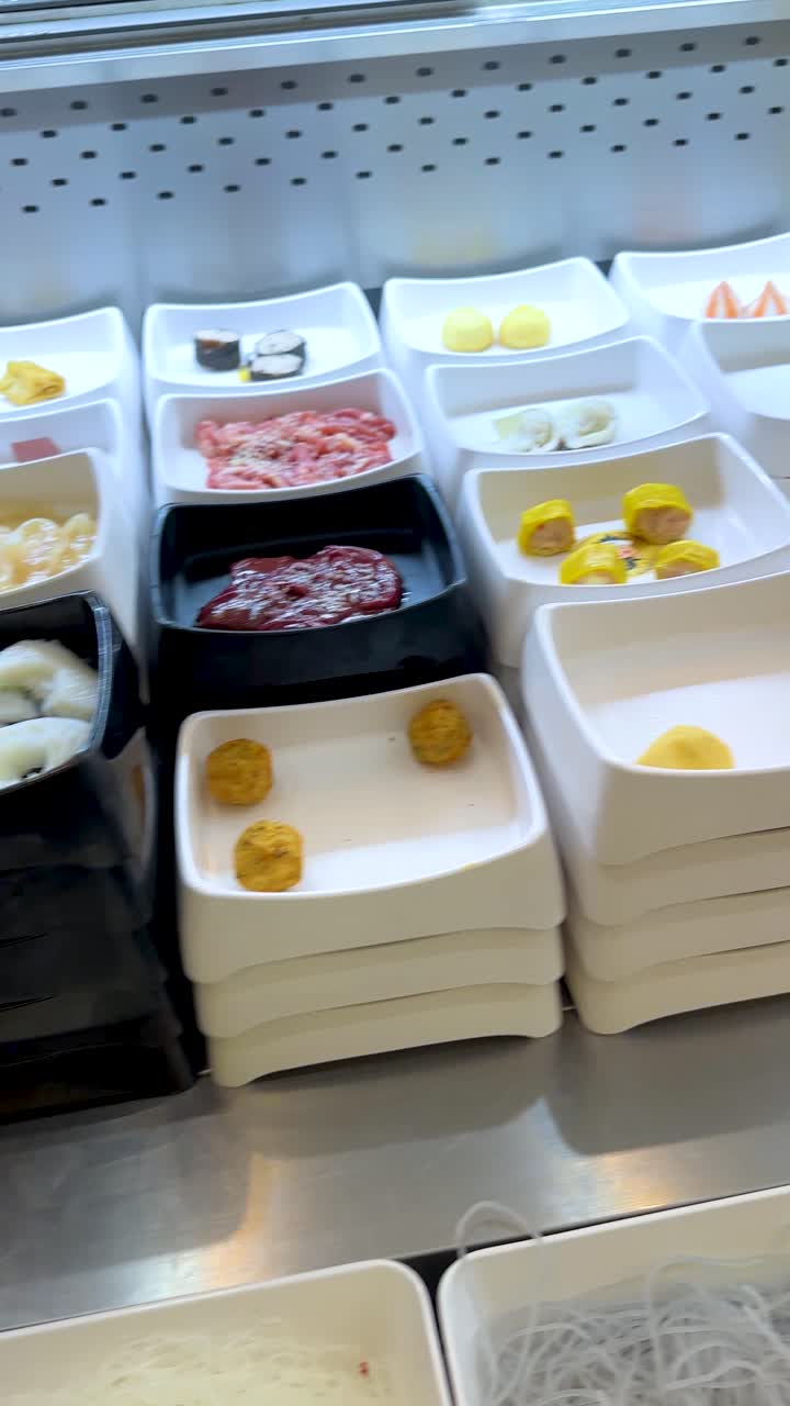 Una telecamera panoramica su scaffali refrigerati che contengono vassoi di carne cruda e ingredienti freschi per buffet