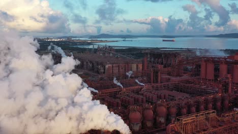 Drohnenaufnahme-Einer-Kohle--Und-Metallfabrik-Bei-Sonnenaufgang,-Die-In-Der-Nähe-Von-Großen-Dampfschornsteinen-In-Betrieb-Fliegt