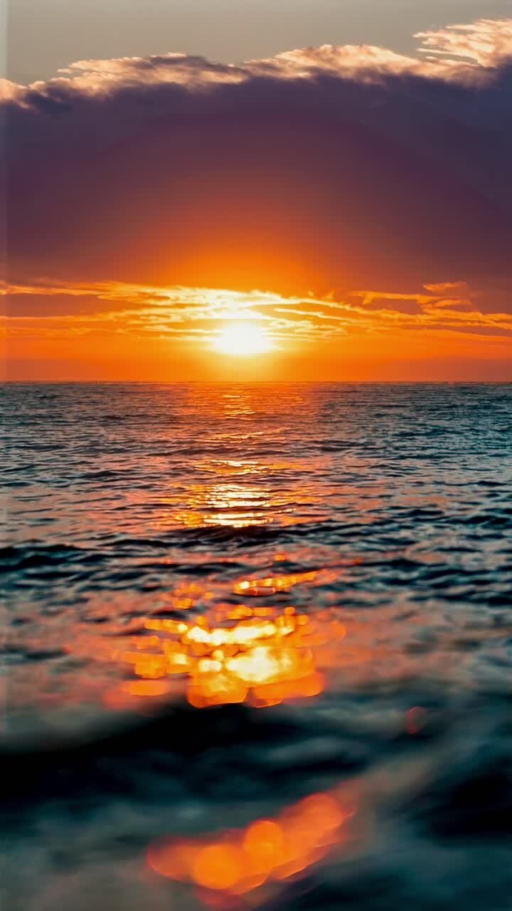 A serene sunset over the ocean, captured from a low angle. The vibrant colors and gentle waves