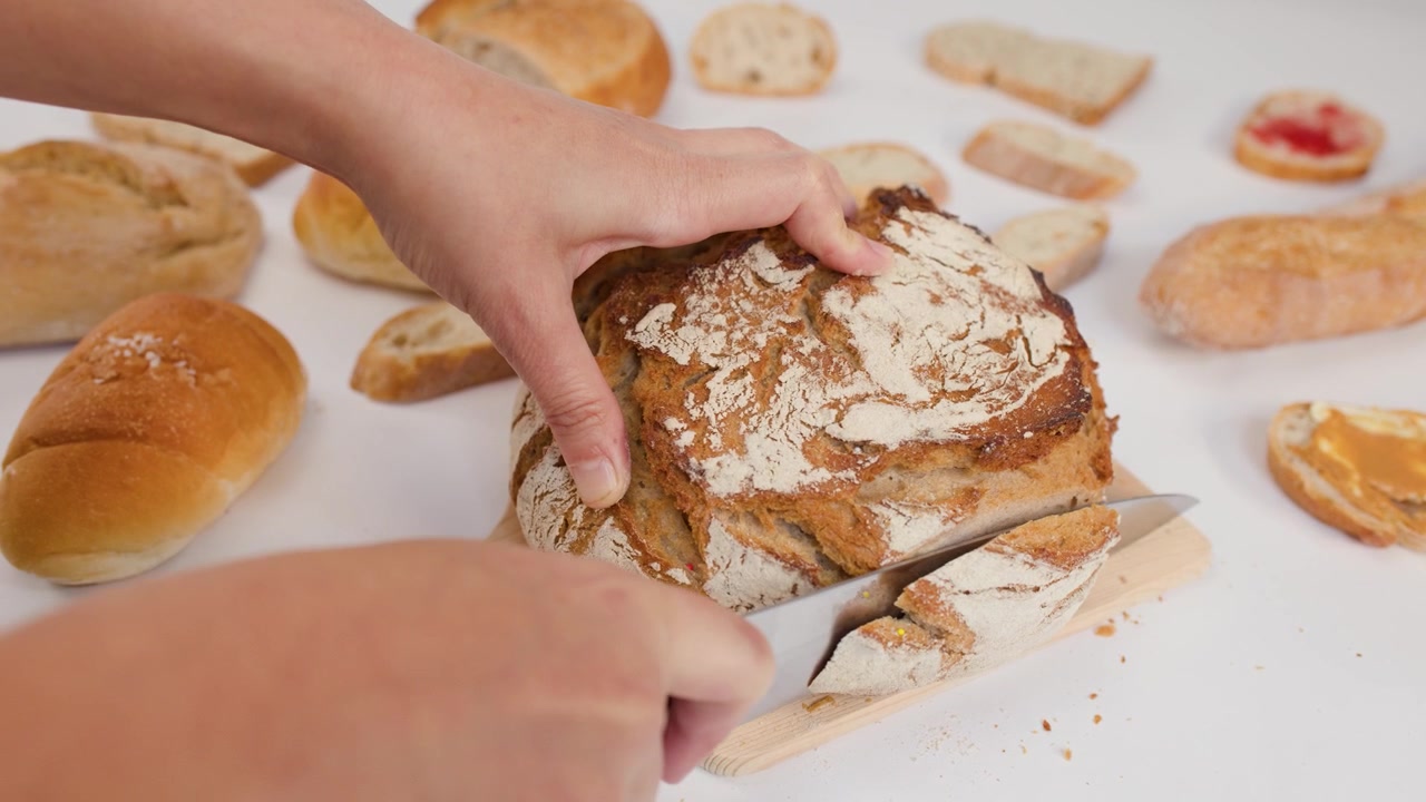 Close-up of hands using a knife to slice crusty artisanal bread on white background.