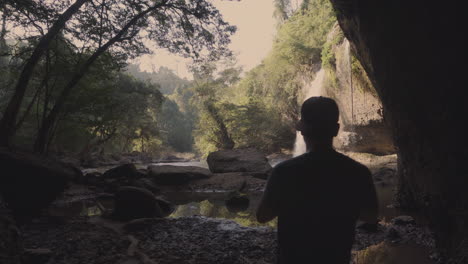 Un-Joven-Fotógrafo-De-Paisajes-Y-Naturaleza-Tomando-Fotos-De-Una-Cascada-Dentro-De-Una-Cueva-Oscura-En-Medio-De-La-Selva-Tropical