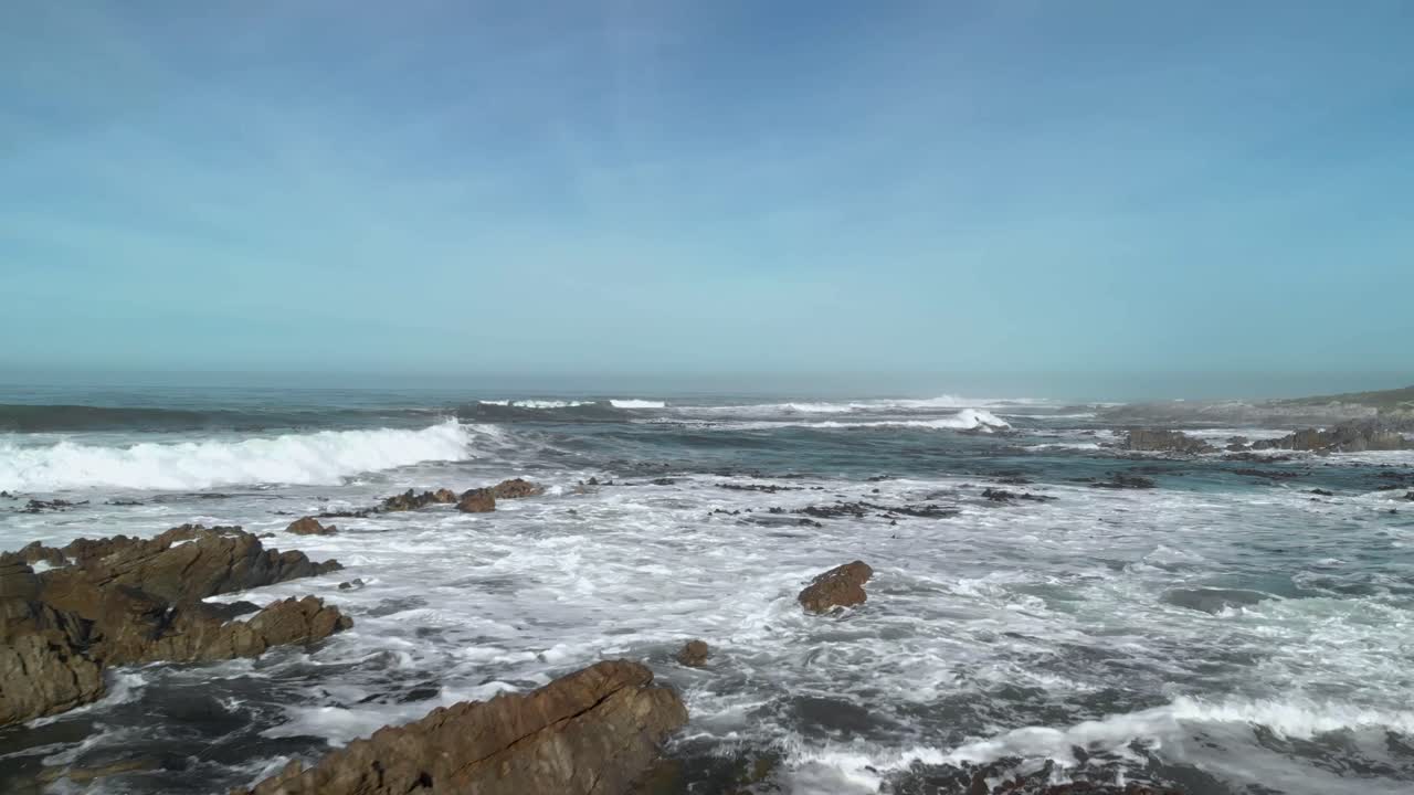 Drone che vola basso sopra i massi su una spiaggia, rivelando onde che si infrangono, maree e bambù mentre prosegue verso il mare aperto.