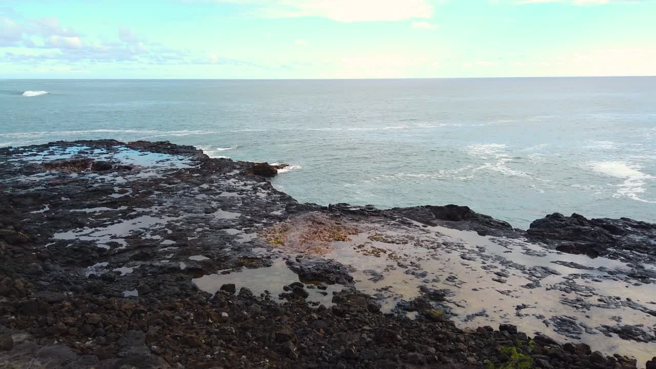 4K Hawaï Kauai, plan statique du geyser marin Spouting Horn jaillissant de manière répétée au centre du cadre, devenant plus puissant à chaque fois, avec de l'eau dans une cavité de roche volcanique à gauche du cadre et des vagues océaniques au loin.