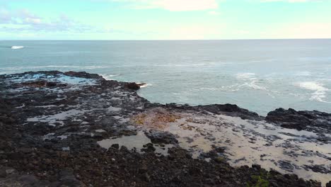 4k hawaii kauai static spouting horn blowhole going off repeatedly in center of frame blowing bigger each time with water in hole in lava rock in left of frame with ocean waves in distance