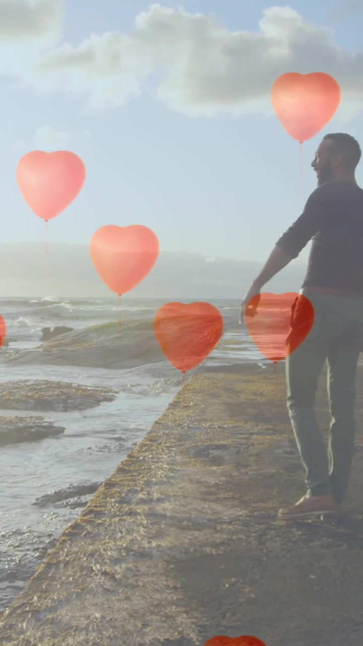 Múltiples globos de corazón flotando sobre una pareja señalando la orilla del mar.