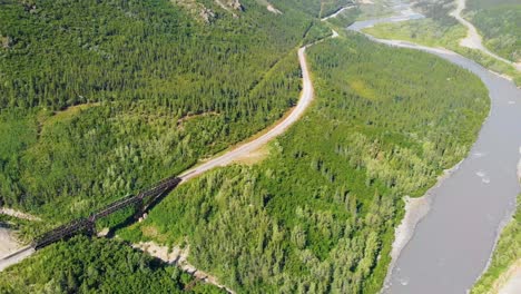 4k drone video of train trestle bridge and mountains rising above the chulitna river near denali national park and preserve, ak during summer