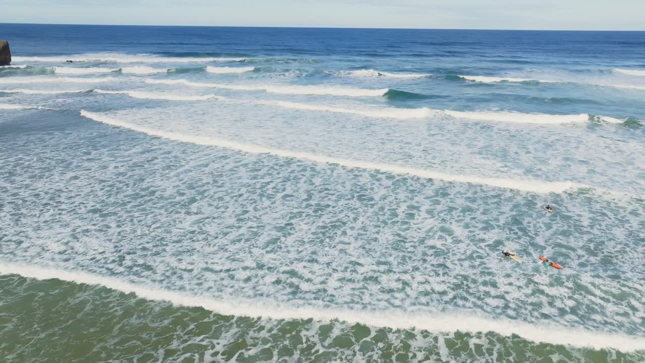 Aerial view of a beach in Portugal with rolling waves, where surfers are learning to ride the waves in a summer's day.