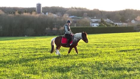 Niña-Montando-Su-Pony-A-Través-Del-Prado-Y-Hacia-La-Puesta-De-Sol